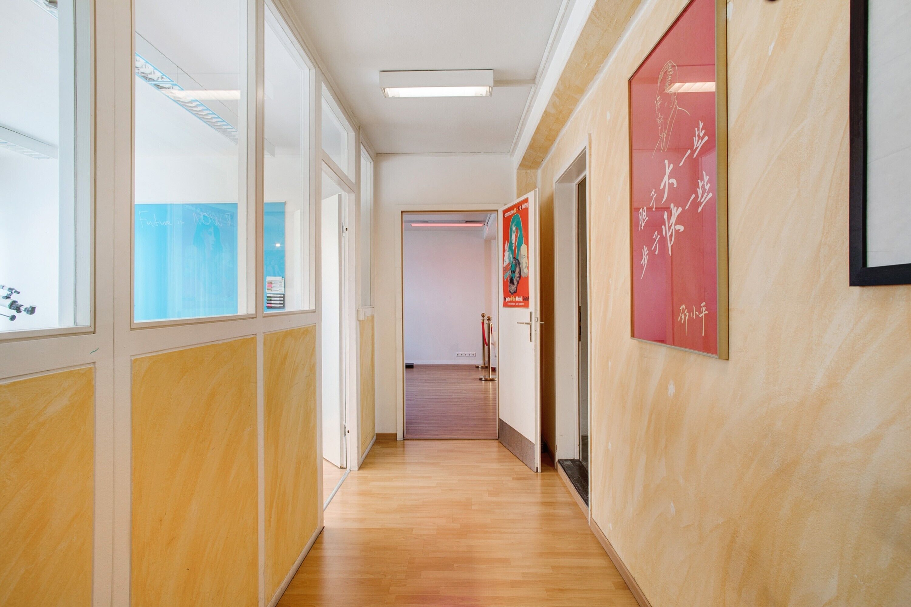 A hallway with wooden flooring, glass doors, and red signage.