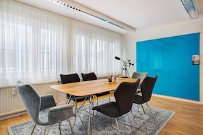 A conference room with a wooden table, six chairs, a telescope, and a blue wall with a chalkboard. - Vacation Home "Commune88 East" with Shared Terrace & Wi-Fi (Friedrichshafen, Germany)