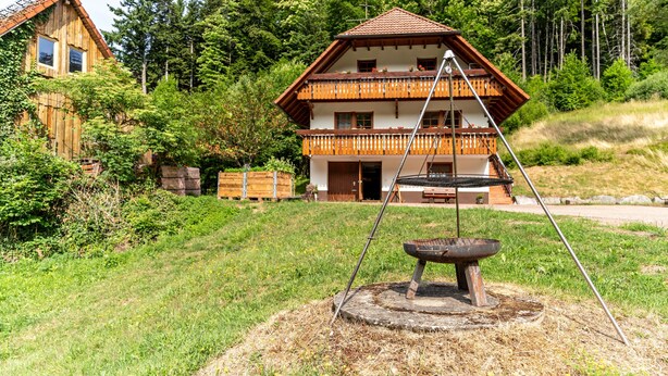 Une maison en bois à deux étages, dotée d’un balcon et entourée de verdure et d’arbres.