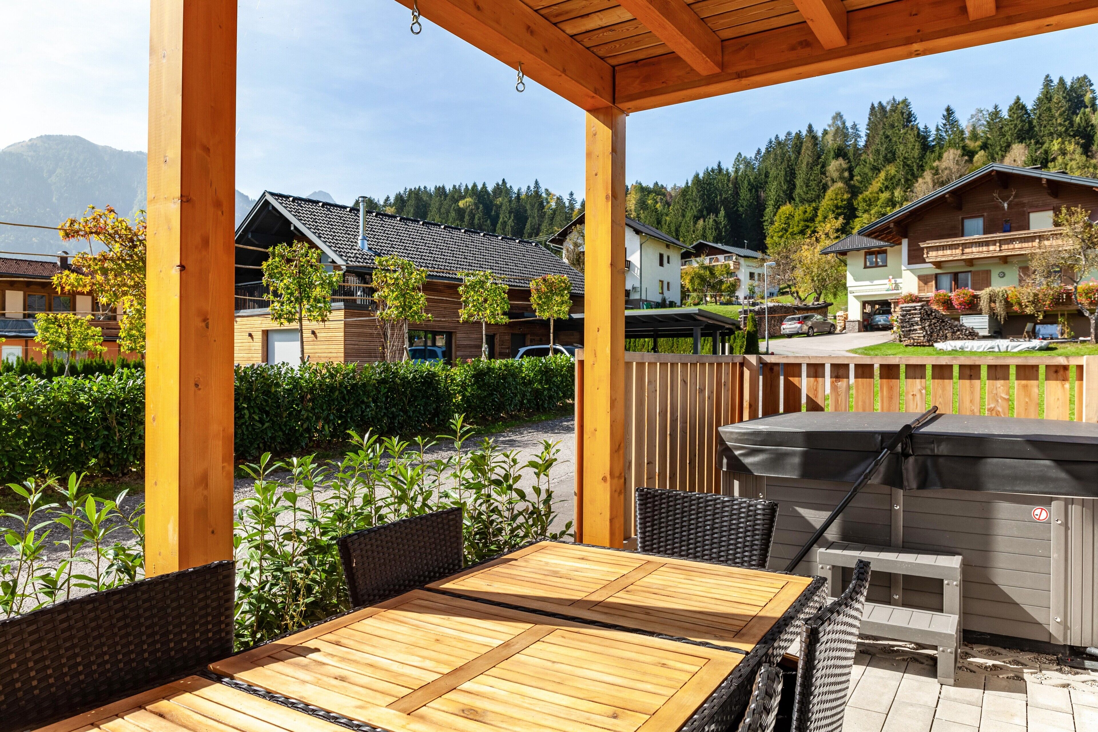 Une terrasse extérieure avec une table et des chaises en bois, un barbecue et une vue sur des immeubles résidentiels et des montagnes.