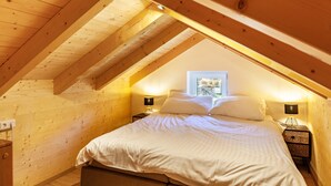 A bedroom with a sloped ceiling, wooden walls, a bed with white bedding, two bedside tables with lamps, and a framed picture on the wall.