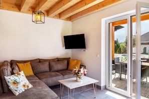 Uma sala de estar com sofá, mesa de centro com um vaso, televisão de tela plana e porta de vidro deslizante para área externa.