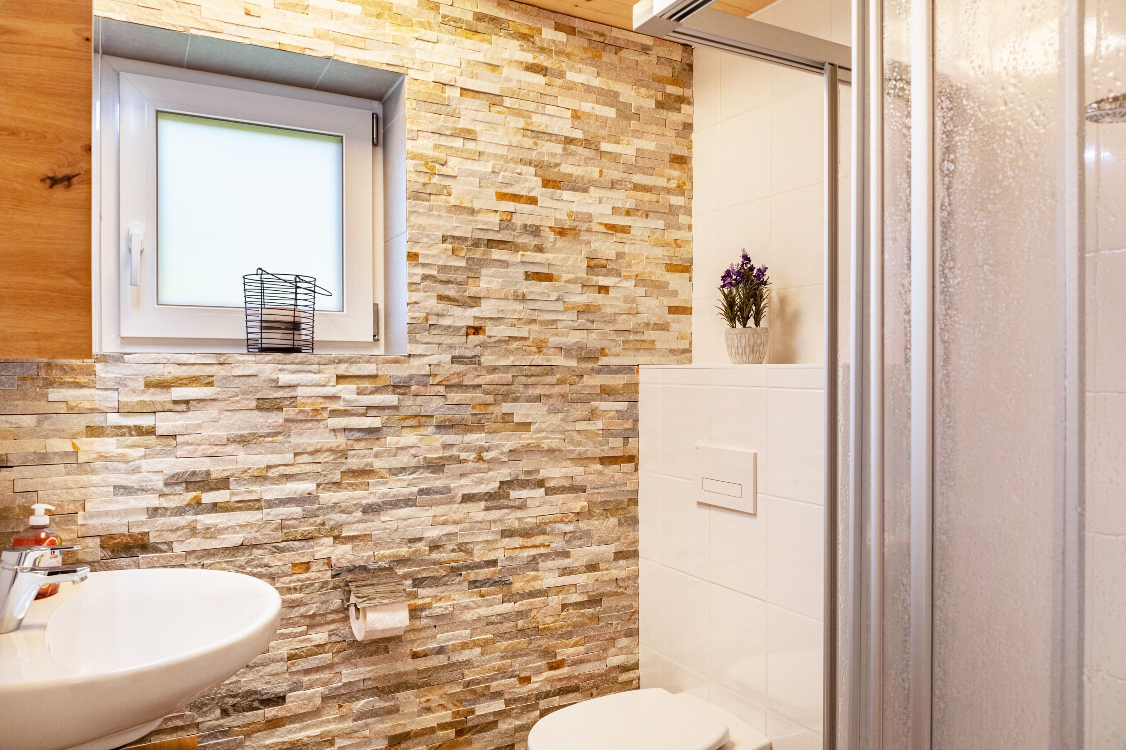 Un bagno con parete in mosaico di pietra, una finestra, un lavandino e un water.