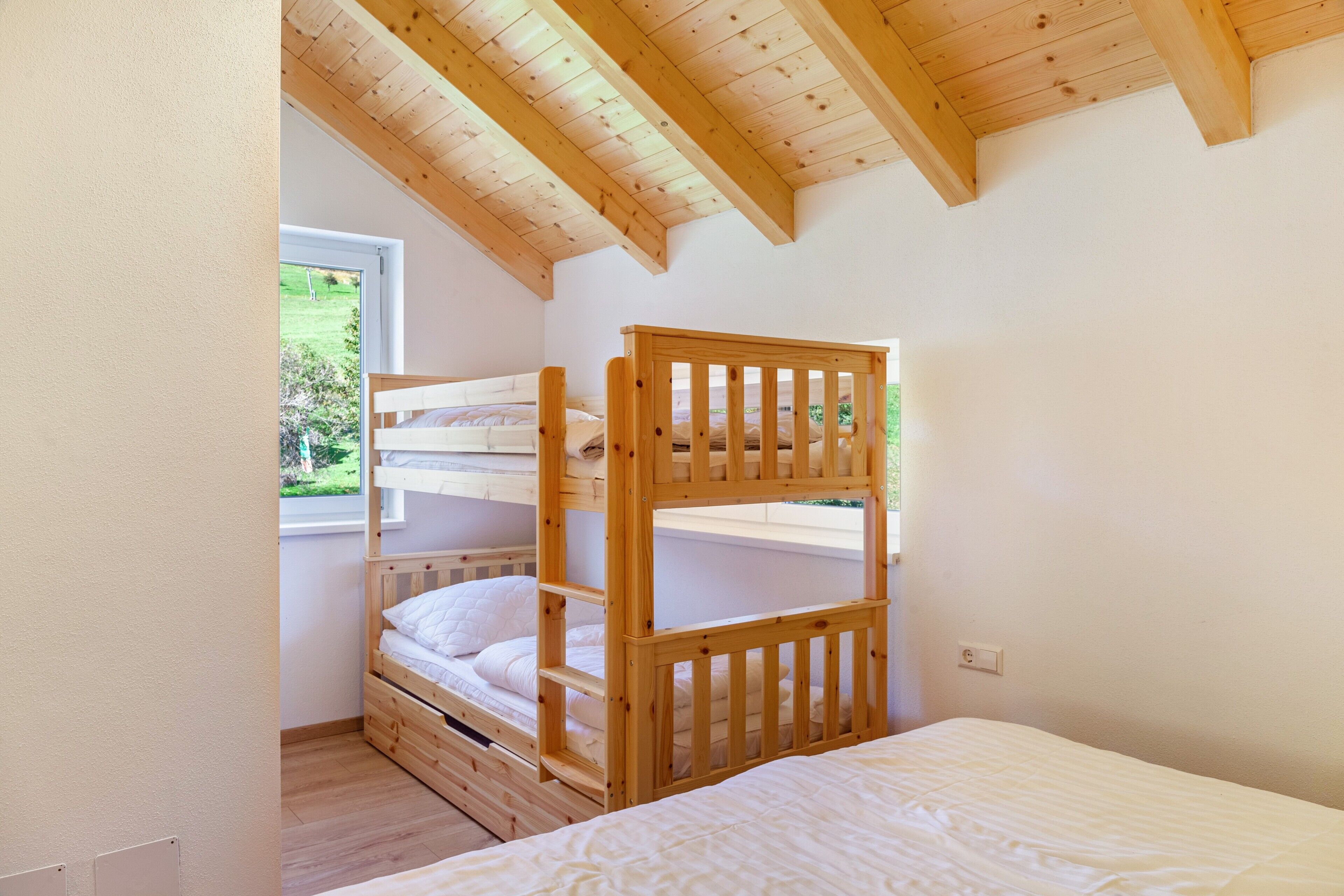 A bunk bed room with a wooden ceiling and a window with a view of greenery.