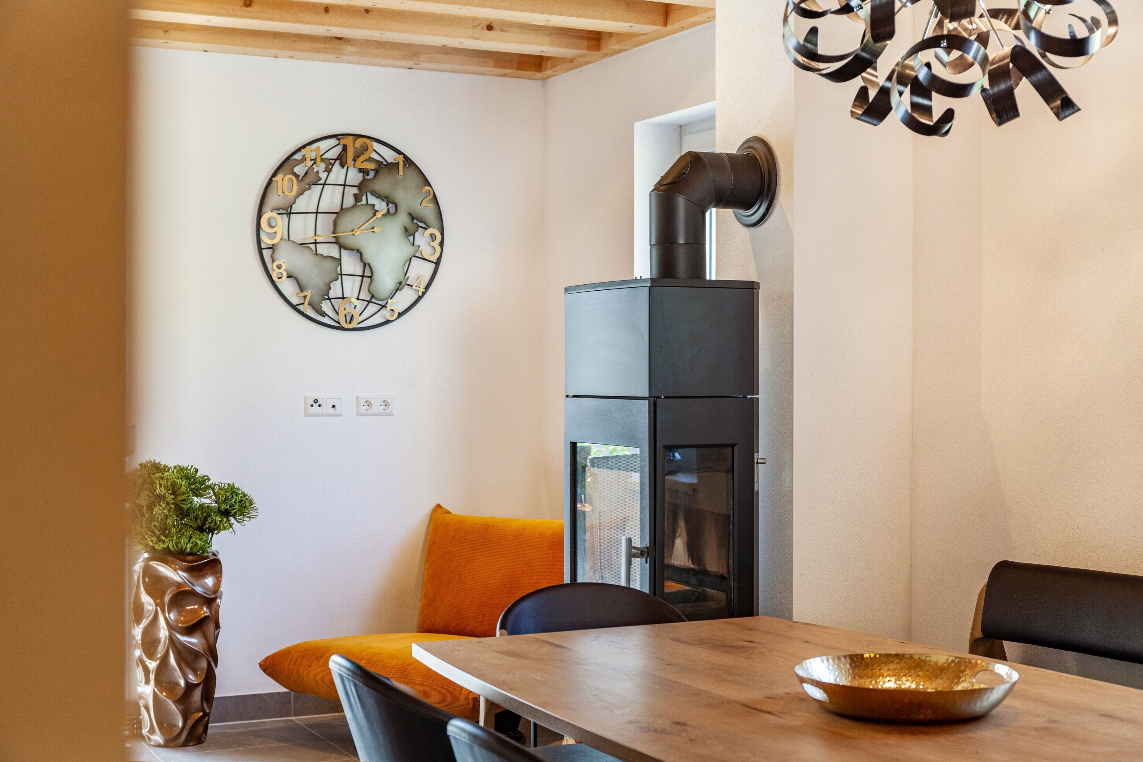 Een modern interieur met een houten plafond, een wandklok, een zwarte kookplaat en een eettafel met stoelen.
