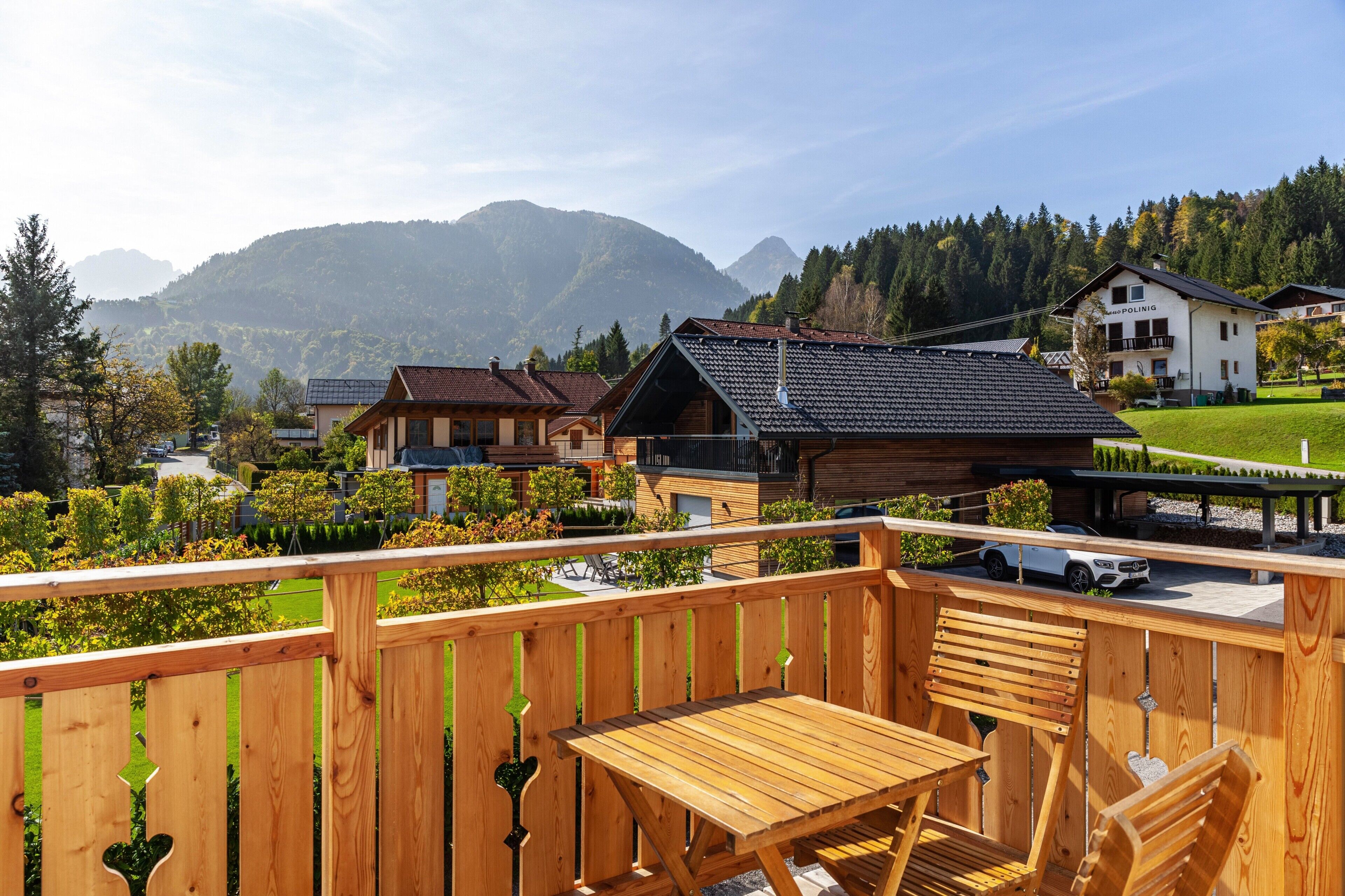 Een houten terras met een tafel en stoelen, met uitzicht op een woongebied met huizen en bergen op de achtergrond.
