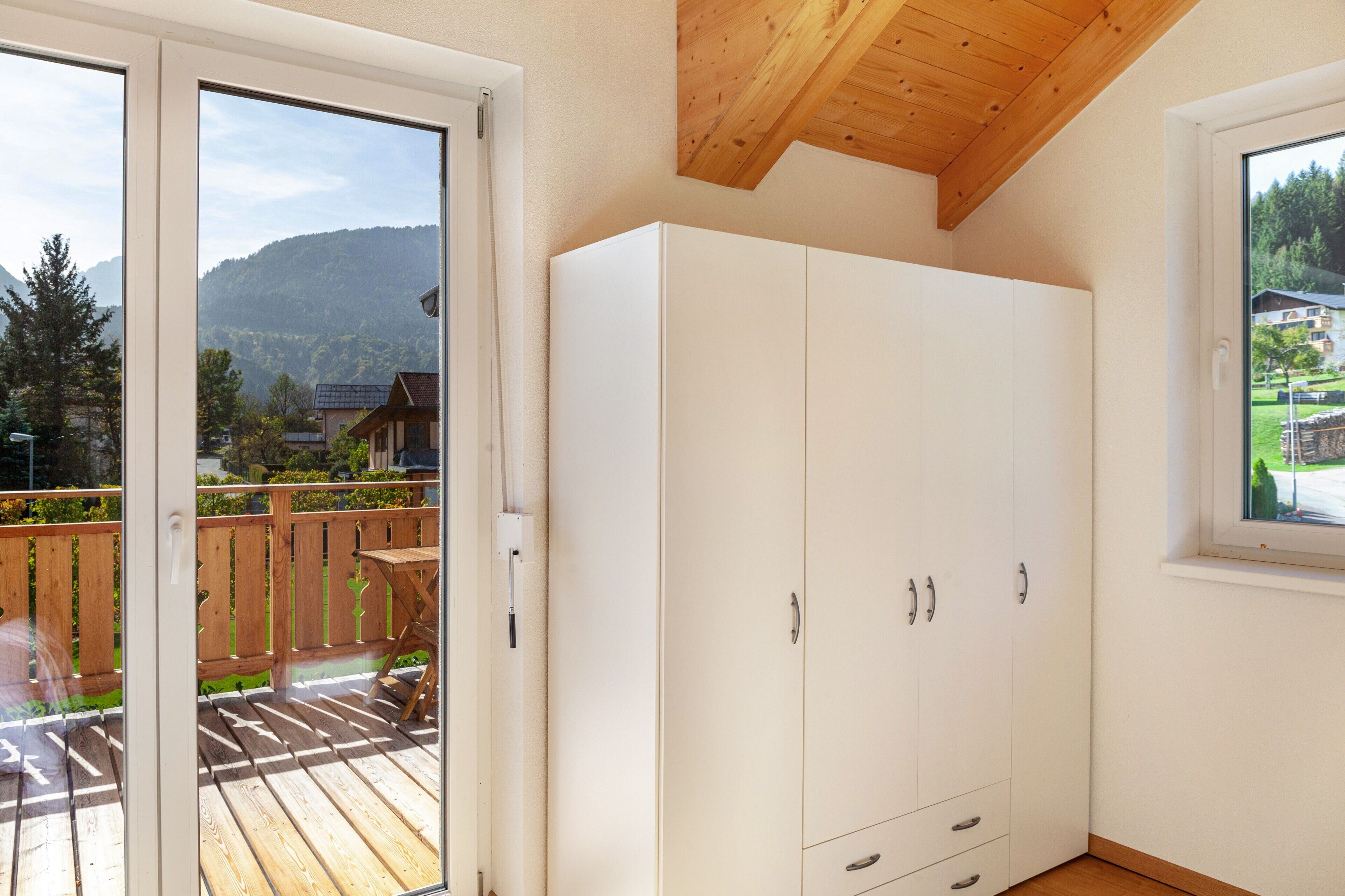 Een kamer met een houten plafond, een witte garderobe en een balkon met uitzicht op bergen.