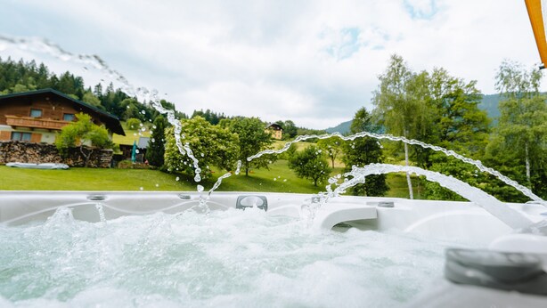 A hot tub with water jets, surrounded by a lush green landscape and a mountain in the background.