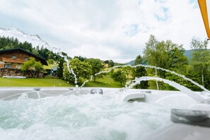 A hot tub with water jets, surrounded by a lush green landscape and a mountain in the background. - Holiday home 'Bubbelen Aan De Piste' with mountain view, terrace, jacuzzi and WiFi (Kötschach)