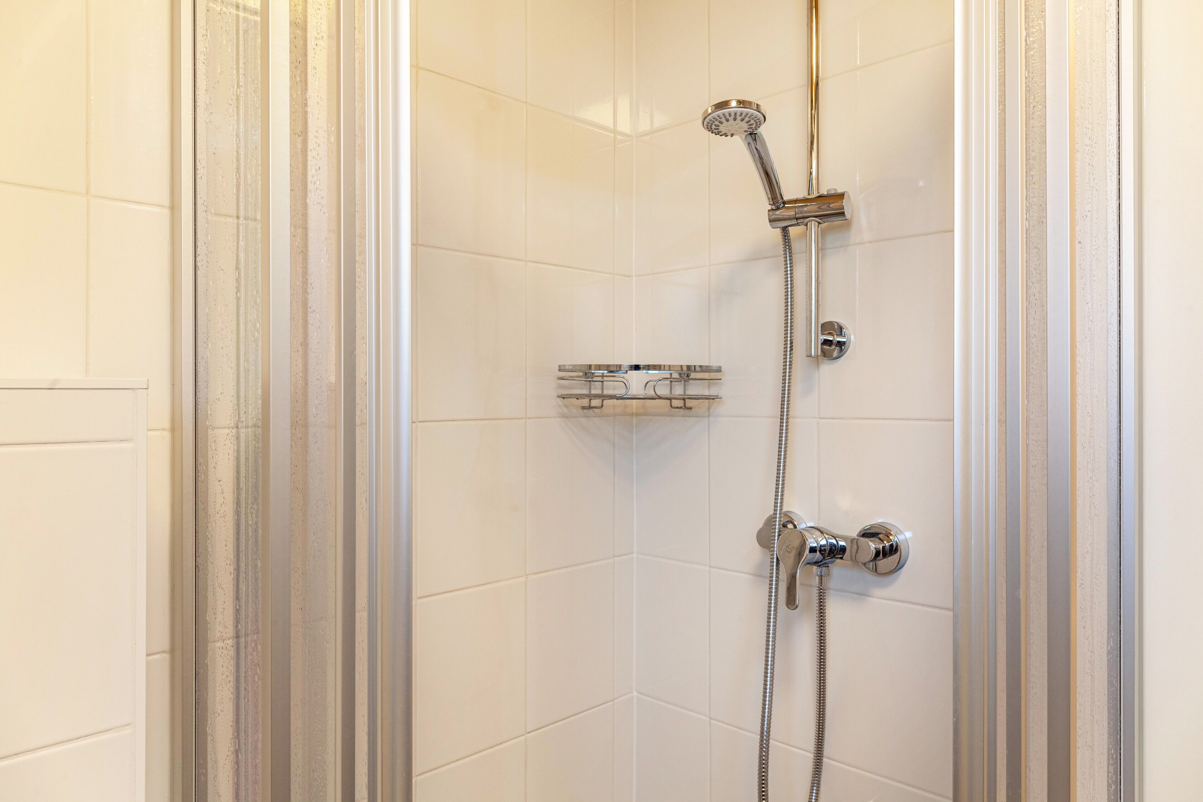 A shower with a handheld showerhead and a wall-mounted faucet.
