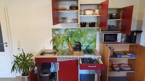 Una cocina compacta con un lavamanos, microondas y diferentes utensilios.