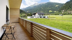 Un balcon avec un plancher en bois, une table avec des chaises et une vue sur une maison et des montagnes.