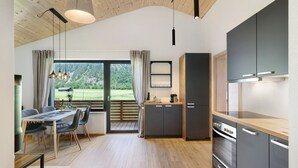 Une cuisine moderne avec un plancher en bois, un coin repas comprenant une table et des chaises, et une vue sur un paysage verdoyant par la fenêtre.