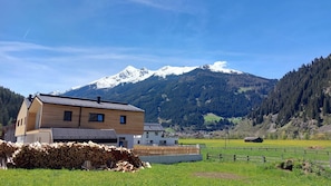 A two-story wooden house with a sloped roof, a stack of firewood in front, and a mountain with snow-capped peaks in the background. - Apartment Stackler54 – Balcony, Mountain View, WLAN (Neustift im Stubaital)