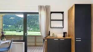 Une cuisine moderne avec un comptoir en bois, une étagère intégrée et une vue sur un paysage verdoyant, visible à travers une porte coulissante.
