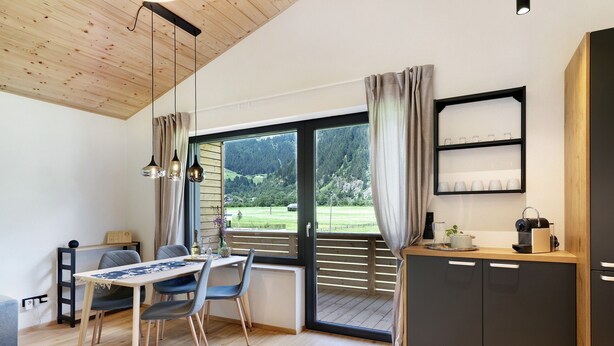 Une cuisine moderne avec un plan de travail en bois, un coin repas comprenant une table et des chaises, et une grande fenêtre donnant sur un paysage verdoyant.