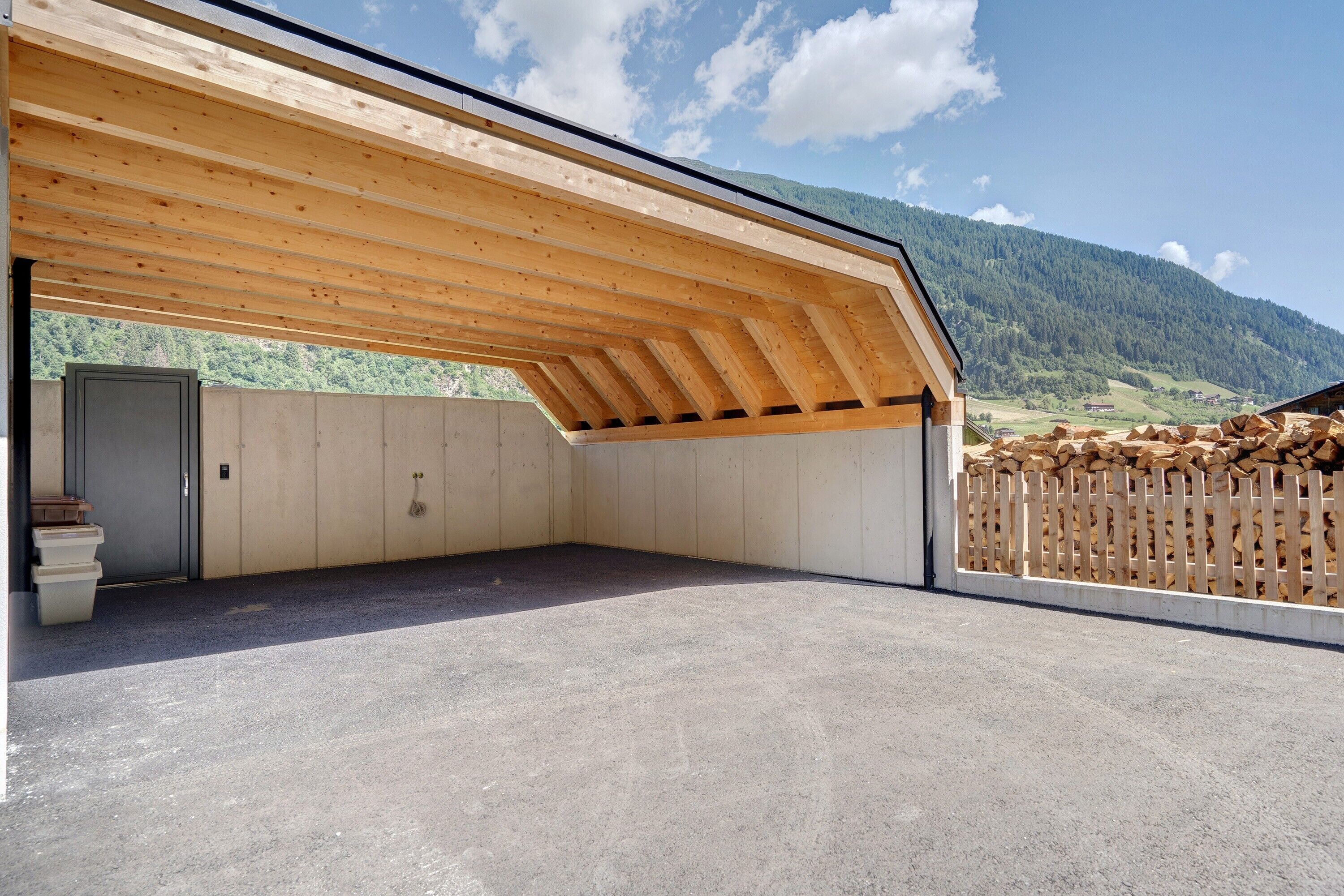 A covered outdoor area with a concrete floor, wooden ceiling, and a view of a mountainous landscape.