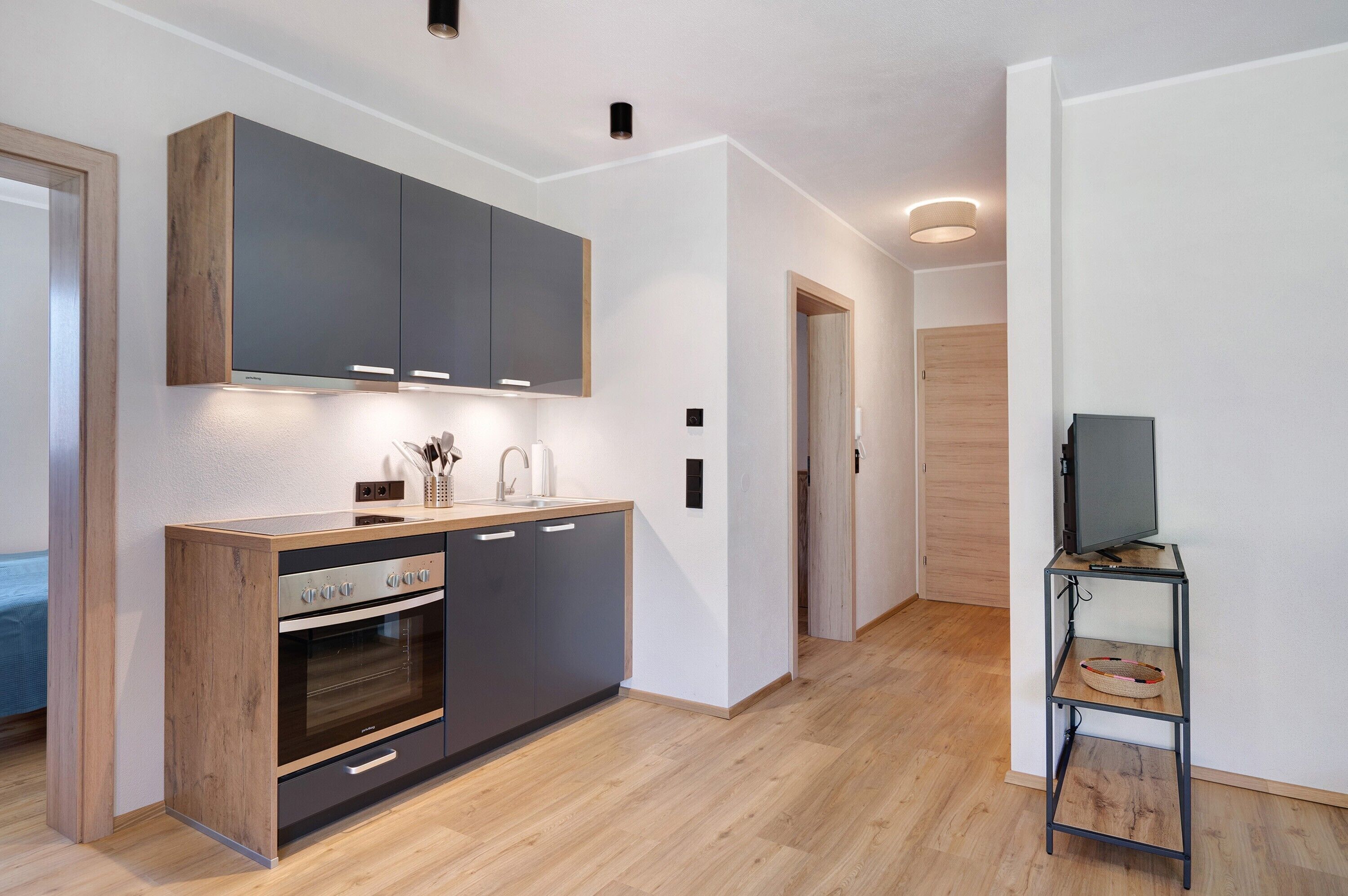 Una cocina moderna con electrodomésticos integrados, encimera de madera y un televisor pequeño sobre un mueble.