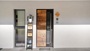 A modern building entrance with a wooden door, a glass door, and a metal shelf with items. - Sleep in Stubaital: Apartment 'Stackler54 - With Garden', Mountain View, Terrace, Wi-Fi (Neustift im Stubaital)