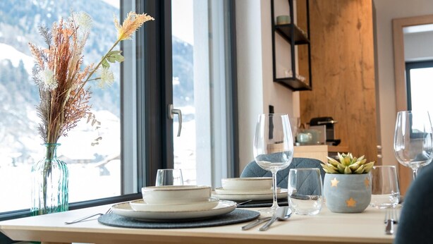 A dining table set with plates, bowls, cutlery, and a vase with dried flowers. - Sleep in Stubaital: Apartment 'Stackler54 - With Garden', Mountain View, Terrace, Wi-Fi (Neustift im Stubaital)