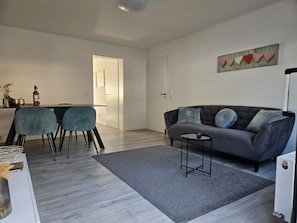 Un salon moderne avec un canapé gris, deux fauteuils bleus, une petite table basse et un tapis gris.