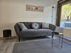 Un canapé gris avec des coussins, un petit tabouret noir, un tapis gris et un décor mural en forme de cœur.