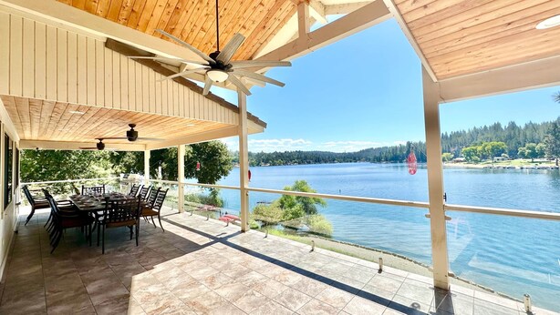 A covered patio with a table and chairs, overlooking a lake with a forested shoreline.