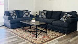 A living room with a dark blue sofa set, a coffee table, and a patterned rug. - Casa Feliz is minutes from Colorado River, Oatman, Casinos, Laughlin. (Fort Mohave)