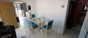 A dining area with a glass table and blue chairs, a white wall, and a door leading to another room. - Casa Completa & Confortável (Foz do Iguaçu)
