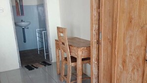 Ein Zimmer mit Holztisch, Stühlen, einem Kleiderschrank und einem Badezimmer mit Waschbecken und Spiegel.