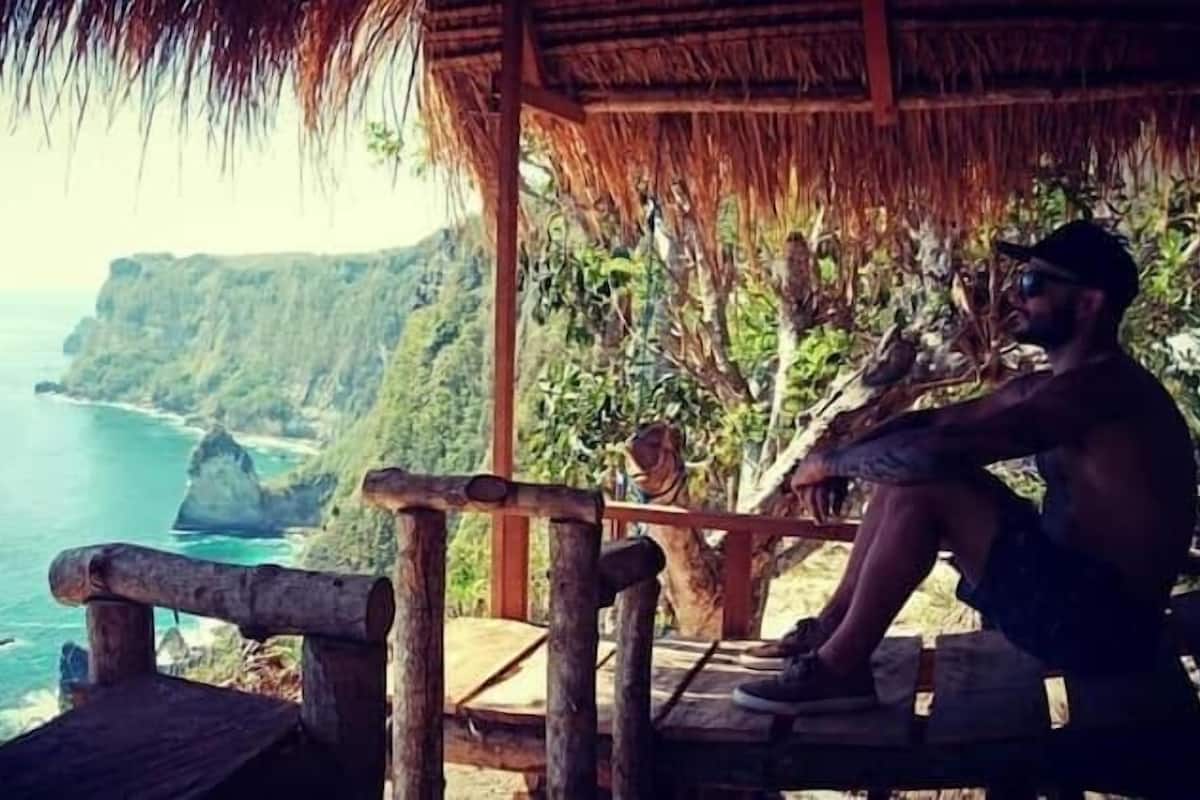 A person sitting on a wooden bench with a view of the ocean and cliffs.