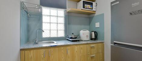 A kitchen with wooden cabinets, a stainless steel refrigerator, a microwave, and a kettle on the countertop.
