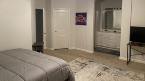 Quarto com cama, ventoinha no teto, porta, banheiro com espelho e televisão.