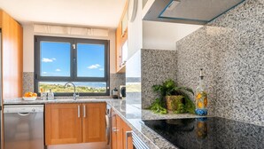 Een keuken met een vaatwasser, houten kastjes, een granieten aanrechtblad, een raam met uitzicht en een decoratieve fles.