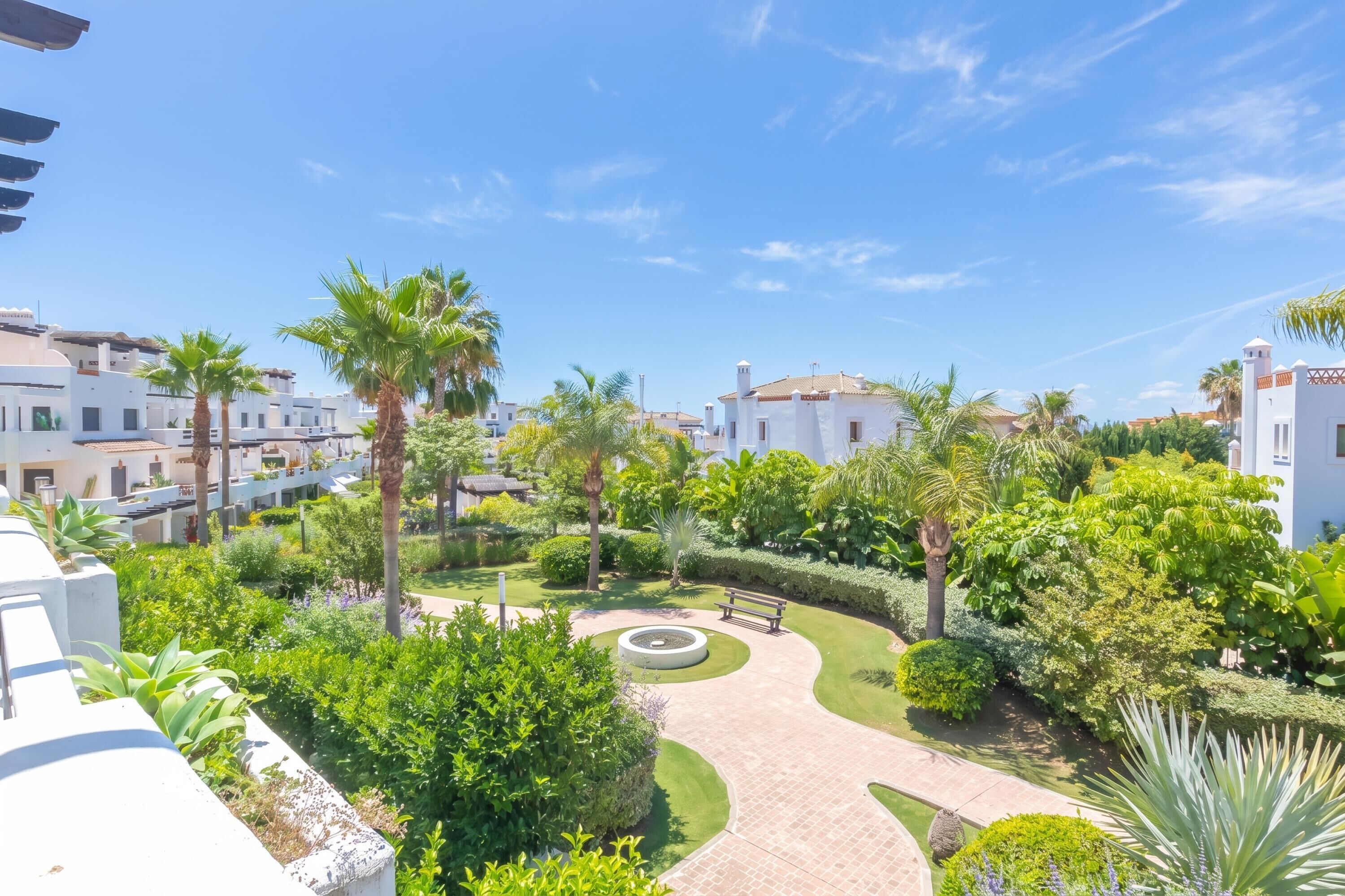 Un patio con palmeras, un jardín circular y edificios blancos.