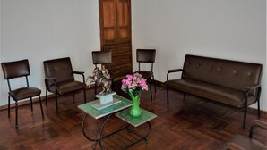 Une pièce avec une porte en bois, deux fauteuils en cuir marron, un canapé marron et une table verte ornée d’une statue et de fleurs.
