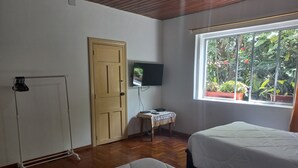 Une chambre avec deux lits, une porte en bois, un téléviseur et une fenêtre donnant sur un paysage verdoyant.