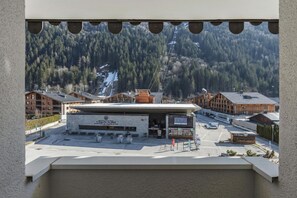 Ein Hotel mit moderner Fassade, einem Parkplatz und einem Bergpanorama im Hintergrund.