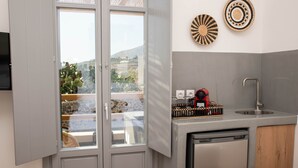 A compact kitchen with a built-in dishwasher, a small sink, and a window overlooking a garden. - Aidani Luxurious Rooms  (Santorini)