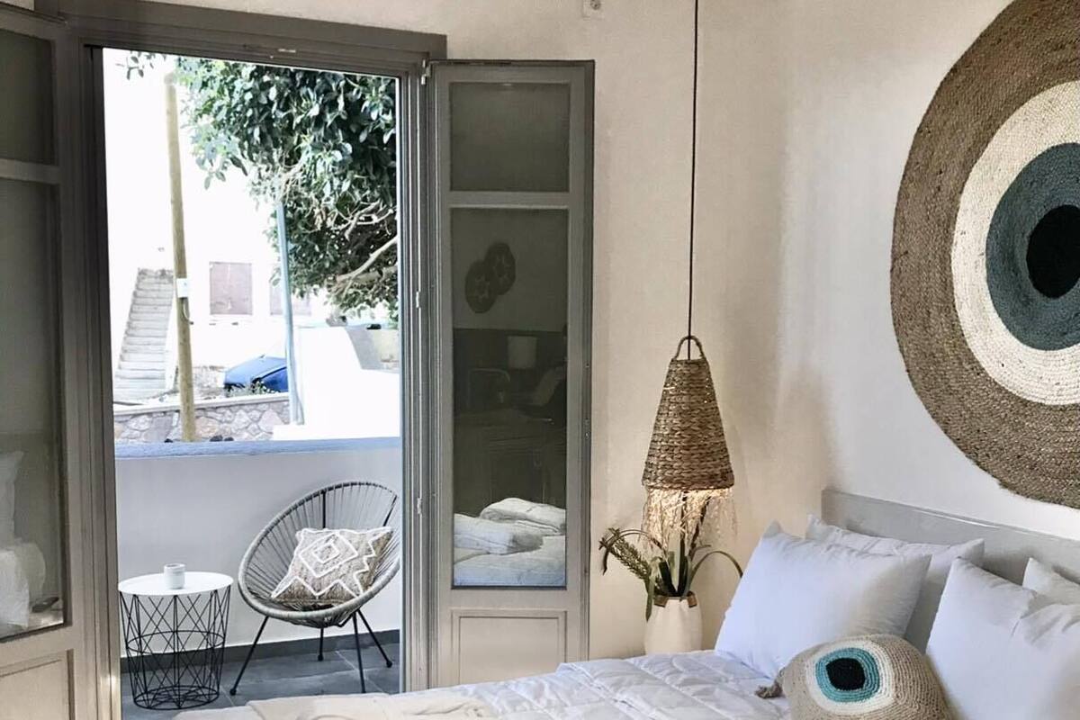 A bedroom with a bed, a chair, a hanging light fixture, and a view of the outside.