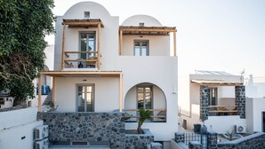 A two-story building with a stone facade, a balcony with a wooden railing, and a small garden area. - Aidani Luxurious Rooms  (Santorini)