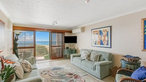 Relax in this stylish living room with a sofa, flat-screen TV, and sliding glass door leading to a balcony with ocean views.