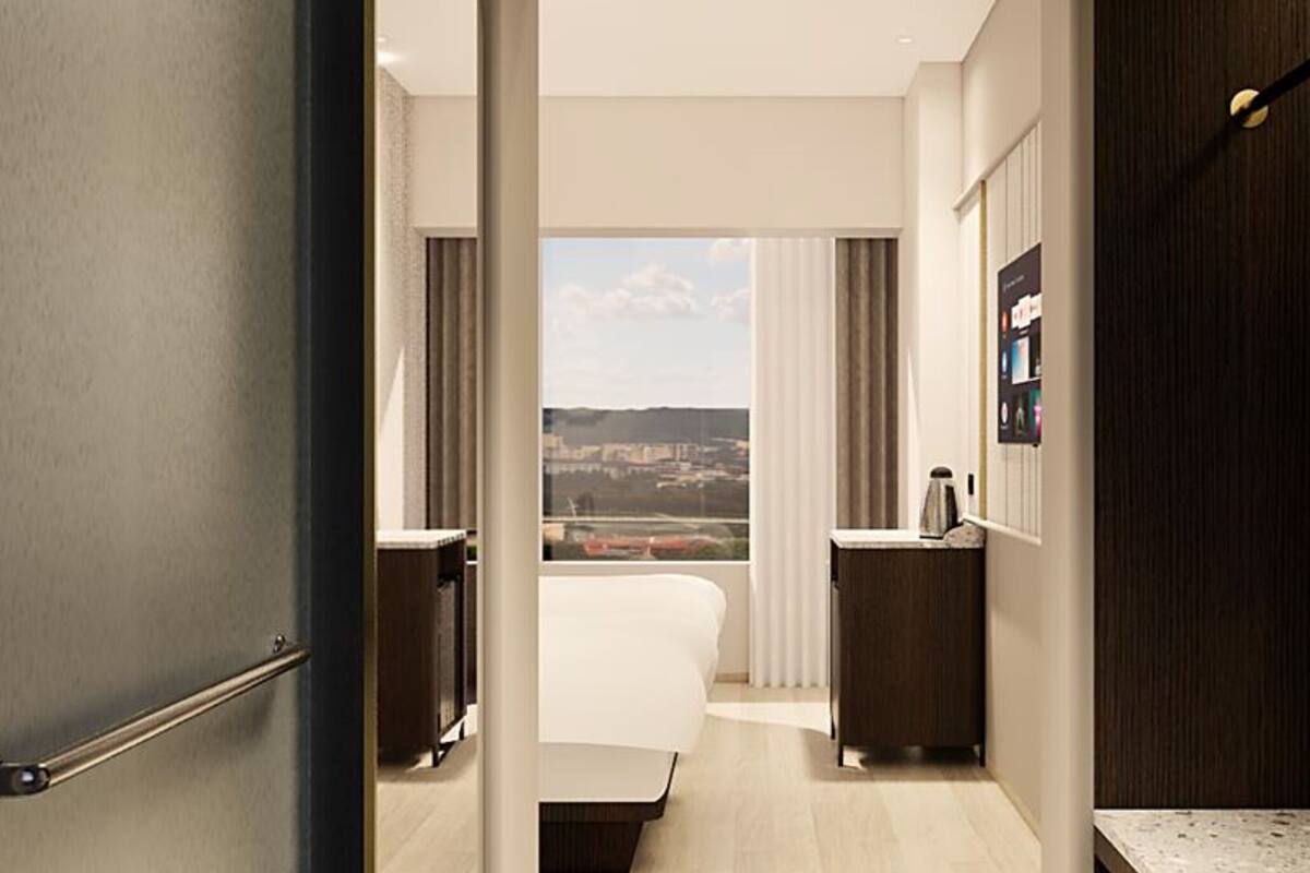 Ein Hotelzimmer mit Bett, kleinem Schreibtisch, Spiegel und Blick auf die Stadt.