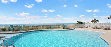A clear blue pool with a wooden deck, lounge chairs, and a view of the ocean.