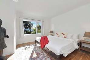 A bedroom with a bed, a nightstand, a lamp, a window with a view, and a statue. - The Bayside Cottage Oceanview Vacation Home (Victoria)