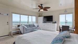 Une chambre avec un grand lit, un ventilateur de plafond, une télévision, un bureau et une vue sur la plage.