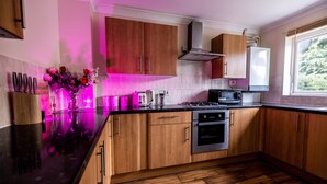 Une cuisine moderne avec des meubles en bois, un plan de travail noir, des appareils en acier inoxydable et une fenêtre donnant sur un paysage verdoyant.