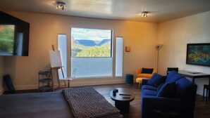 A modern room with a bed, a blue sofa, a desk, and a large window with a mountain view.