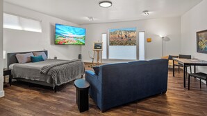 A modern, well-lit room with a bed, sofa, and dining area.