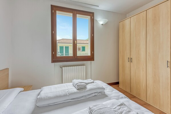 A bedroom with a large wardrobe, a bed with white linens, a window with a view of buildings, and a ceiling light. - Porto Letizia Venezia 7, Porlezza, Italy (Porlezza)